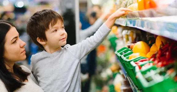 Une femme et un enfant parcourant des légumes dans un supermarché, inspectant soigneusement les produits frais exposés.